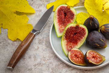 Feigen reif geschlossen aufgeschnitten mit gelbem Feigenblatt auf Teller mit Messer