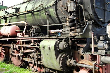 Historic railway. The front part of a steam locomotive. A fragment of the boiler, wheels, pistons, lantern and bumper are visible.