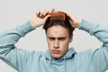 Close-up photo. A strange young man combs his hair in a light light blue hoodie, a place in the background for inserting an advertising layout.Horizontal Studio photo