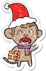 shouting hand drawn distressed sticker cartoon of a monkey carrying christmas gift wearing santa hat
