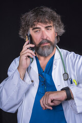 doctor dressed in the blue surgical suit and white coat consulting a mobile phone