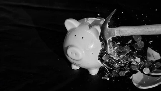 1000fps slow motion clip of a hammer smashing a piggy bank open to spill the coins it contains; financial concept