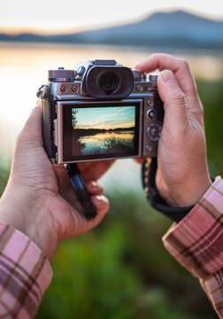 Hand holding a mirrorless digital camera prepare for take a landscape photo. Hands taking photo of sunset with camera