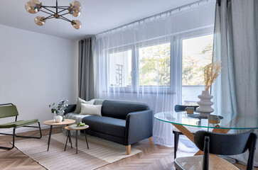 Stylish living room with window and curtains, comfortable furniture with sofa and armchair and table with chairs . Modern interior of room in apartment.