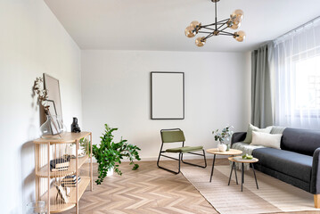 Interior of modern living room in apartment with sofa, armchair and furniture. White wall with empty frame and wooden floor with parquet.