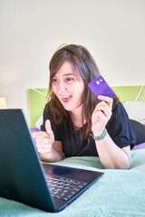 Vertical shot of a young white Caucasian girl doing a transaction with a bank card and a laptop