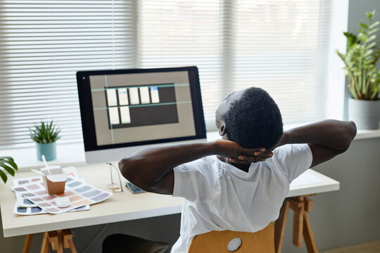Back view of tired black man stretching muscles at office workplace while working in IT