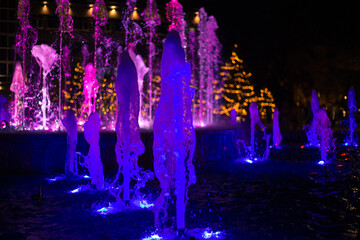 Multicolored illuminated fountain jets in the dark, selective focus, bokeh. Festive background