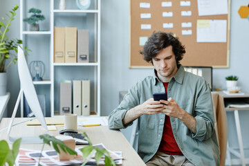 Portrait of Caucasian young man using smartphone at workplace and scrolling social media during...