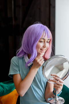 Young Teen Girl With Purple Hair Looking In To A Mirror At Home