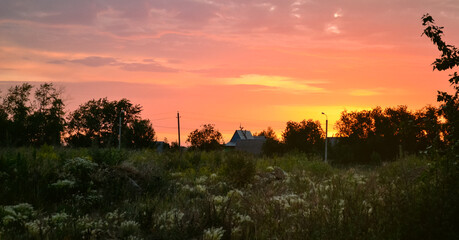 Bright beautiful orange sky at dawn over trees, a house and a grassy field
