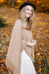Happy and beautiful woman in a brown poncho in the middle of the autumn yellow forest.
