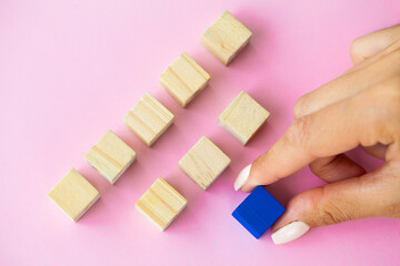 Wooden blocks with a human hand placing one cube at the top on pink background.