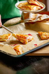 woman transfers ready-made biscuits with cherries to a plate from a baking sheet on a table at home