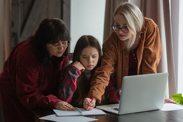sister and mother teaches her teen daughter at home at computer sitting at table