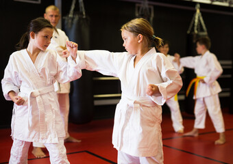 Young girls and boys in kimono and belts sparring during karate training.