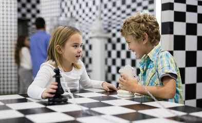 Fototapeta premium Boy adn girl solving puzzle together in quest room stylized like chessboard