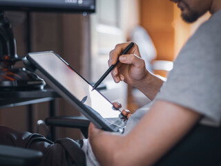 A caucasian guy sits in a work chair and chooses a menu by moving a black pen on a tablet