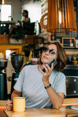 Stylish fifty yeart old woman with mobile phone sits in cafe