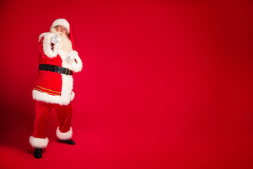 Full length photo of real Santa Claus annoucing big xmas sale on a red studio background, pointing to the camera. Merry Christmas and Happy New Year! A lot of copy space