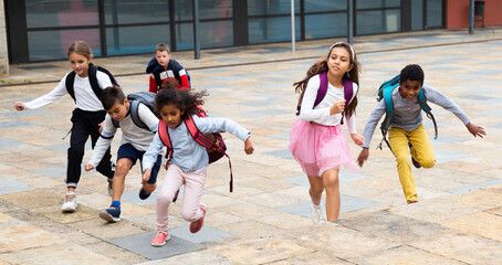 Portrait of cheerful tween boys and girls with school backpacks running in schoolyard in spring day.