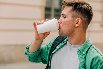 Portrait of a stylish young man in green shirt who drink a takeaway cup coffee