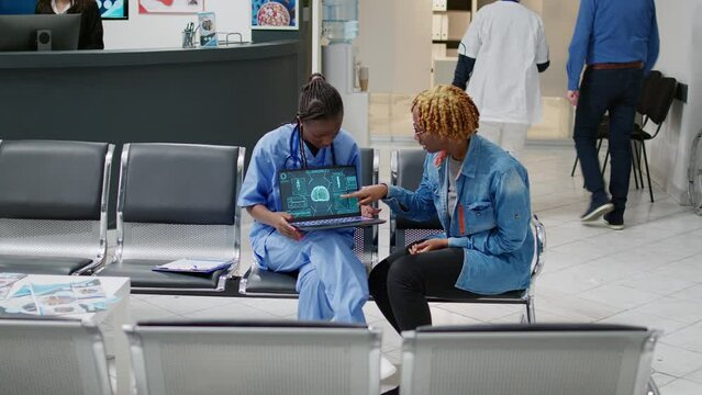 Medical specialist explaining brain diagnosis on tomography to young patient in waiting area. Showing neurology scan, neuroscience and neural system on laptop to woman at healthcare center.