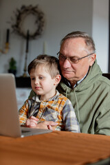 Fototapeta na wymiar Little boy and grandfather using laptop computer at home