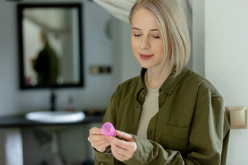 blond hair woman with menstrual cup stands at home