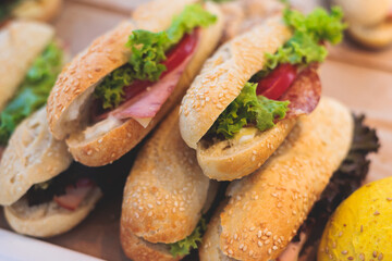 Beautifully decorated catering banquet table on event with different food snacks and appetizers setting with bagel and sandwiches, triange, baguette club submarine sandwich, on a wooden plate