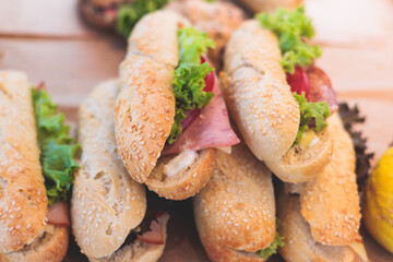 Beautifully decorated catering banquet table on event with different food snacks and appetizers setting with bagel and sandwiches, triange, baguette club submarine sandwich, on a wooden plate