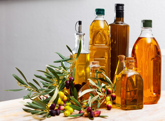 Fresh olive oil in bottles with olives on branches on wooden table