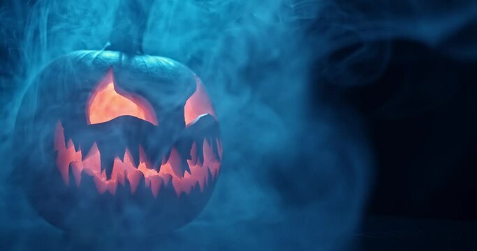 Spooky Halloween jack o lantern with glowing scary face carved out of a pumpkin and surrounded by smoke and mist.