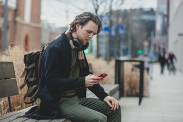 stylish guy in scarf and coat hold mobile phone in a hand at street of Wroclaw, Poland