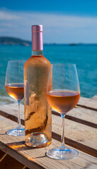 Glasses and bottle of cold rose wine from Provence served outdoor on wooden yacht pier with view on blue water and white sandy beach Plage de Pampelonne near Saint-Tropez, France