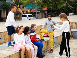 Group of smiling children sitting on stairs and chatting together sitting at urban street