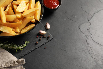 Plate with tasty baked potato wedges, rosemary, garlic and sauce on black table, above view. Space for text