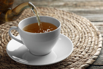 Pouring green tea into white cup with saucer on table, closeup