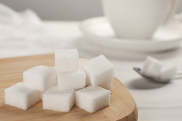Fototapeta na wymiar Refined sugar cubes with wooden board on table, closeup