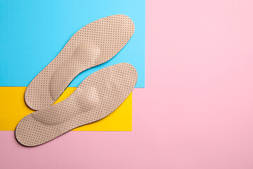Pair of beige orthopedic breathable insoles on color background, flat lay. Space for text