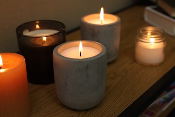 Fototapeta na wymiar Lit candles in different holders on wooden table indoors