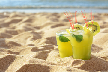 Glasses of refreshing drink with kiwi and mint on sand near sea. Space for text