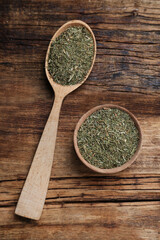 Bowl and spoon of dried dill on wooden table, flat lay