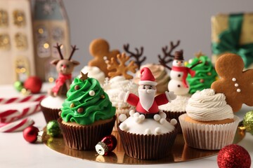 Different beautiful Christmas cupcakes and baubles on white table