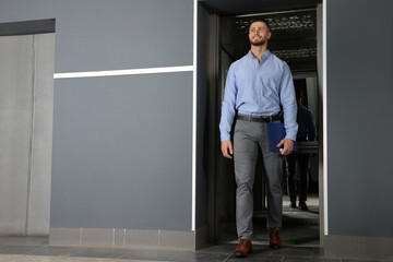 Attractive young businessman walking out modern elevator