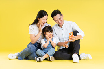 Naklejka na ściany i meble Image of Asian family sitting together happy and isolated on yellow background