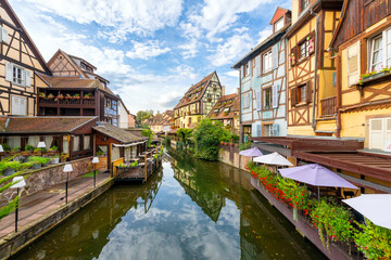 Colorful half timbered buildings and waterfront cafes on the Lauch River in the historic medieval Little Venice district of Colmar, France, in the Alsace region. - obrazy, fototapety, plakaty