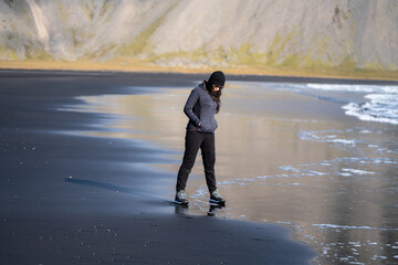 portrait woman walking on the black volcanic sand beach with mountains in the background. She is wearing glasses and cap