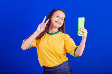 young girl, soccer fan from Brazil. holding cellphone, selfie, self portrait. Smartphone....