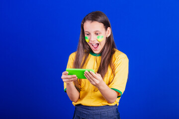 young girl, soccer fan from Brazil. holding cellphone, surprised. Smartphone. applications.